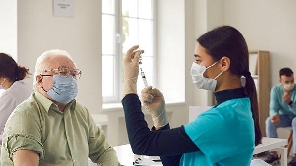 Image of a female healthcare professional giving an older man a Covid-19 vaccination in an aged care setting