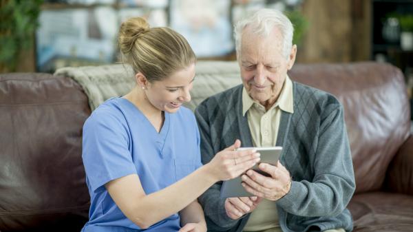 Image of a female care provider with an older man seated on a leather couch.