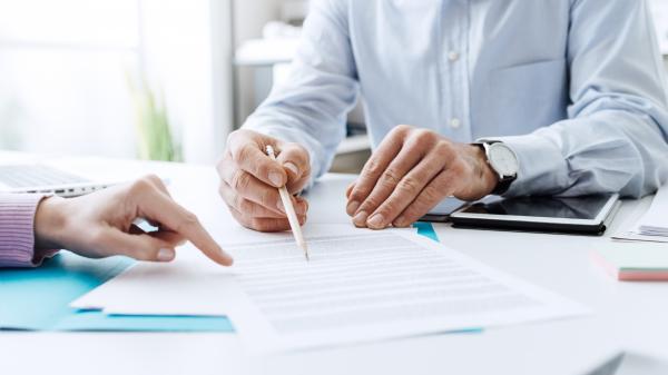 Image of two people at a desk with pens and paper working in an office.